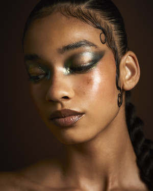 BIPOC Model mit grün-schimmerndem Augen Make Up vor braunem Hintergrund im Rahmen der Weleda x The Face art Academy Kampagne